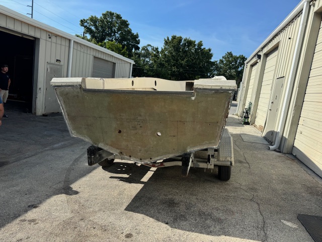 Same boat transformation: sanded and faired hull on its trailer outside the Harper Marine Services shop, prepped for full exterior paint after structural repairs.